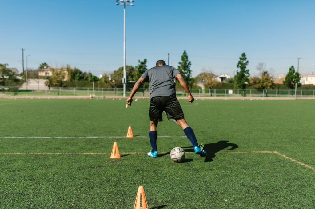 A soccer player practicing drills on a sunny day on an outdoor field.